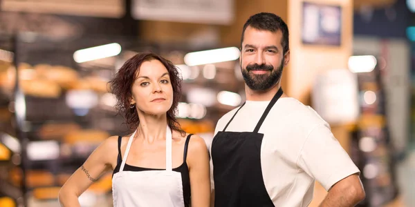 Couple of cooks posing with arms at hip and smiling
