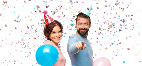 Pareja Con Globos Sombreros Cumpleaños Señala Con Dedo Con Una —  Fotos de Stock