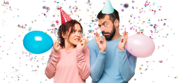 Casal Com Balões Chapéus Aniversário Com Dedos Cruzando Desejando Melhor — Fotografia de Stock