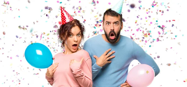 Casal Com Balões Chapéus Aniversário Surpreso Chocado Emoção Facial Expressiva — Fotografia de Stock