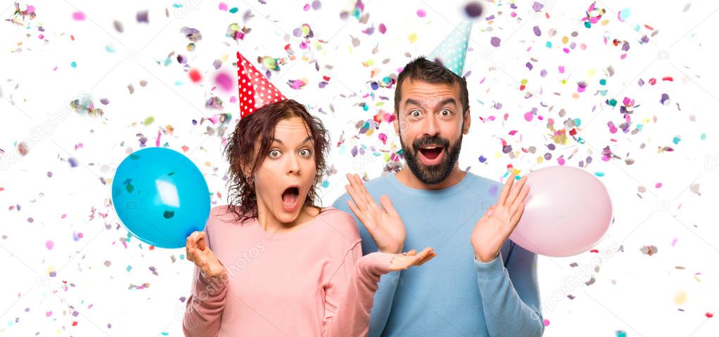 couple with balloons and birthday hats with surprise expression because not expect what has happened with confetti in a party
