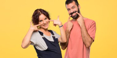 Hamile kadınla ağız parmak ile izole sarı zemin üzerine işaret ederken hoş bir ifade ile gülümseyen çift