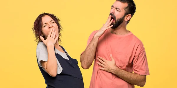 あくびと手で口を覆っている妊娠中の女性とカップルします 分離された黄色の背景で眠そうな表現 — ストック写真