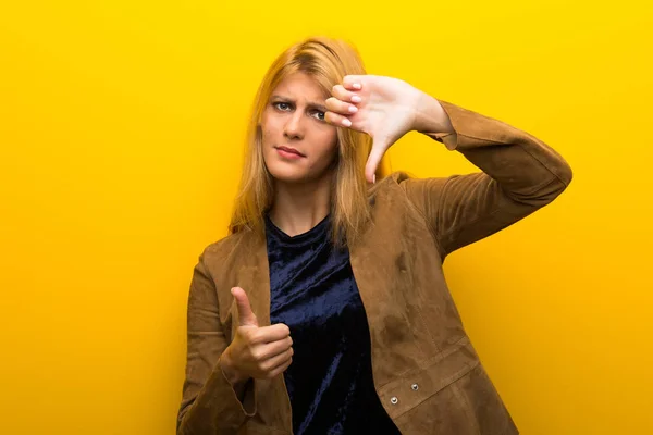 Blonde girl on vibrant yellow background making good-bad sign. Undecided between yes or not