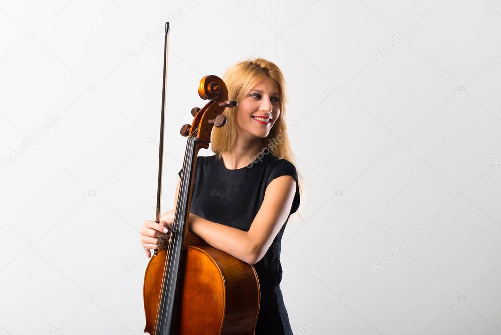 Young blonde girl with her cello posing on white wall