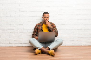 Afrika kökenli Amerikalı adam çene üzerinde el ile seyir onun laptop ile katta oturan