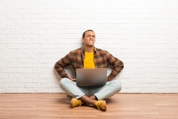 African american man sitting on the floor with his laptop suffering from backache for having made an effort