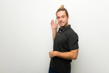 Geri işaret ve bir ürün sunan beyaz duvarın üzerinden uzun saçlı sarışın adam