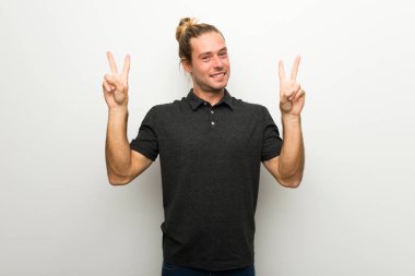 Gülümseyen ve iki elini zafer işaretiyle gösterilen beyaz duvarın üzerinden uzun saçlı sarışın adam