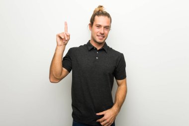 Gösteren ve en iyi iz içinde parmak kaldırma beyaz duvarın üzerinden uzun saçlı sarışın adam