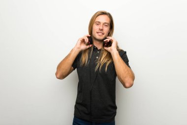 Kulaklıklar ile beyaz duvarın üzerinden uzun saçlı sarışın adam