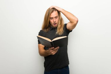 Beyaz duvar bir kitap okuma tadını çıkarırken sürpriz üzerinde uzun saçlı sarışın adam