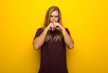 Sessizlik jest belirtisi gösteren sarı duvarın üzerinden uzun saçlı sarışın adam