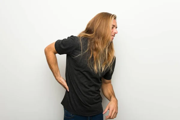 Blond man with long hair over white wall suffering from backache for having made an effort