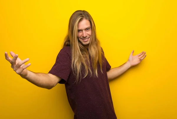 Blond man with long hair over yellow wall proud and self-satisfied in love yourself concept