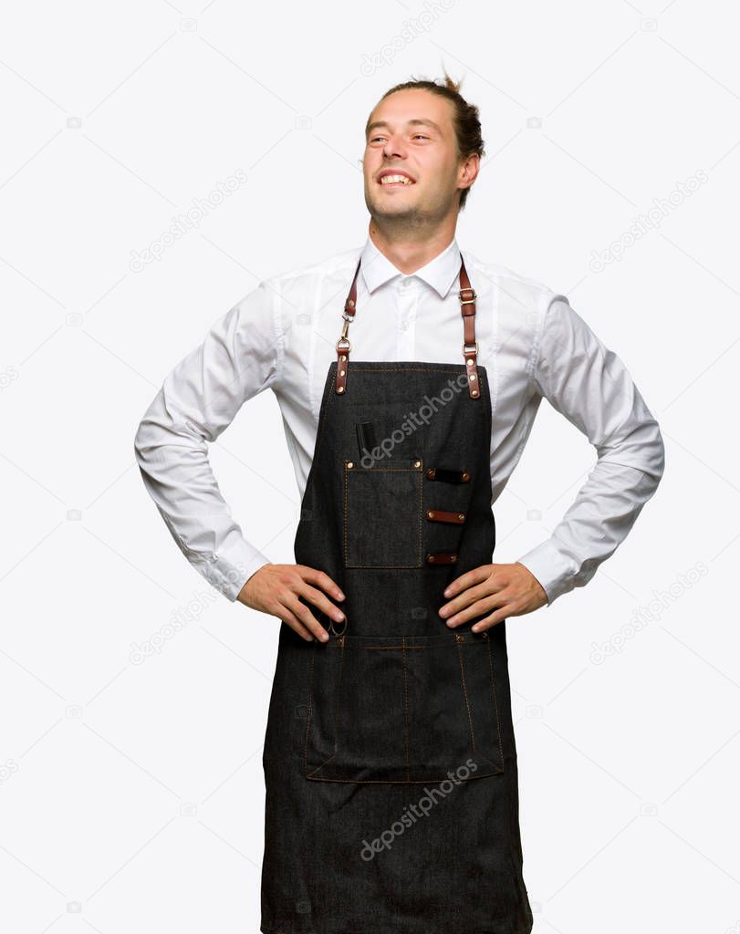 Barber man in an apron posing with arms at hip and laughing on isolated background
