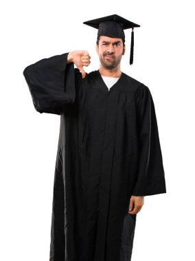 Başparmak aşağı negatif ifade işaretiyle gösterilen onun mezuniyet günü üniversite adamı. Üzgün ifade izole beyaz arka plan üzerinde