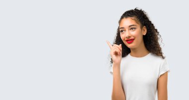Young girl with curly hair standing and thinking an idea pointing the finger up on grey background