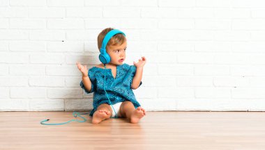 Adorable little baby listening music on white brick background