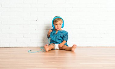 Adorable little baby listening music on white brick background