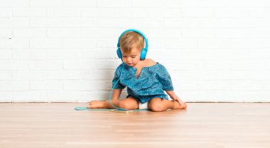 Adorable little baby listening music on white brick background