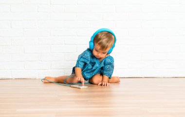 Adorable little baby listening music on white brick background