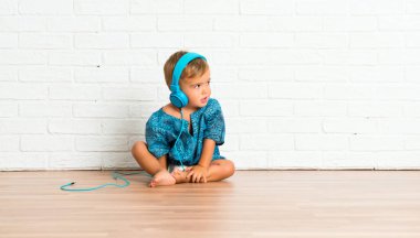 Adorable little baby listening music on white brick background