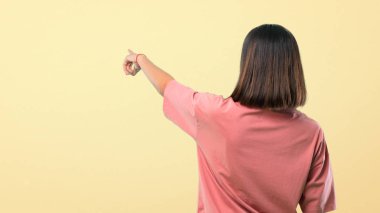Pembe gömlek geri bir ürün arkadan sarı arka plan üzerinde sunulması işaret parmağı ile işaret ile genç kız