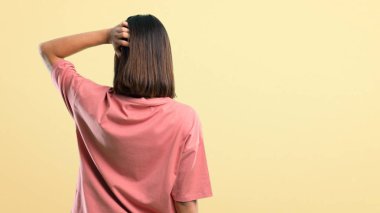 Pembe gömlekli genç kız sarı arka plana bakıyor.