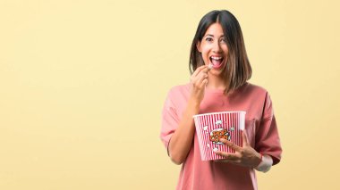 Genç kızla mutlu pembe gömlek popcorns sarı arka plan üzerinde yemek