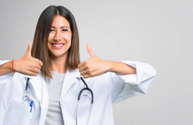 Doktor kadın hareketi Yaşasın vererek ve çünkü gülümseyen stetoskop ile gri arka plan üzerinde başarı elde etti