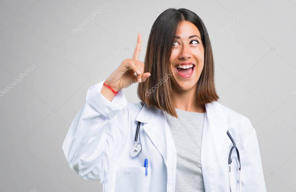 Doctor woman with stethoscope intending to realizes the solution while lifting a finger up on grey background