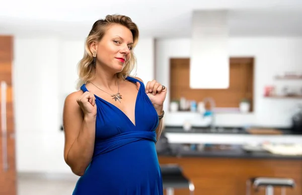 誇りと自己満足で青いドレスで金髪妊婦が彼女の家で自分のコンセプトを愛する — ストック写真