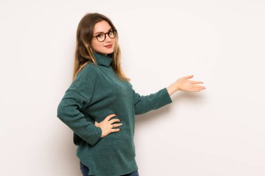 Genç kız geri işaret ve bir ürün sunan beyaz duvar üzerinde