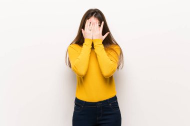 Young woman with yellow sweater covering eyes by hands and looking through the fingers