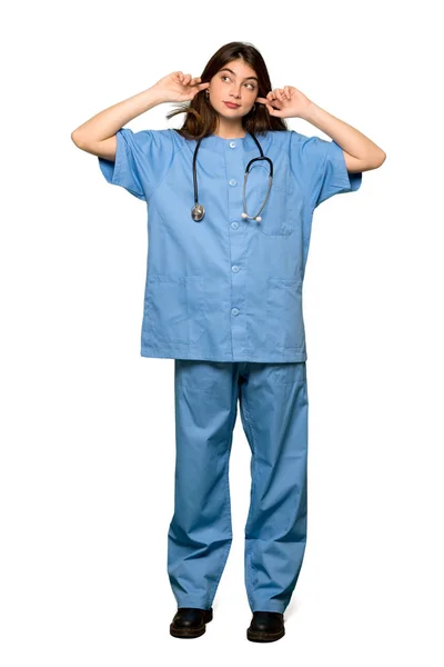 分離の白い背景の上の手で両耳を覆う若い看護師のフルレングスのショット — ストック写真