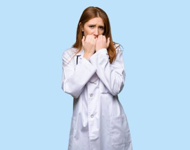 Kızıl saçlı Doktor biraz gergin ve korkmuş koyarak ellerini ağzına izole mavi zemin üzerine bir kadındır