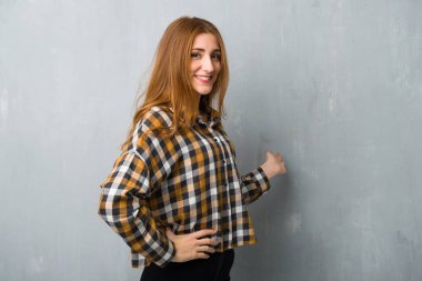 Genç Kızıl saçlı kız geri işaret ve bir ürün sunma grunge duvarın üzerinden
