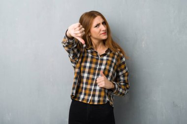 Başparmak aşağı negatif ifade işaretiyle gösterilen grunge duvarın üzerinden genç Kızıl saçlı kız