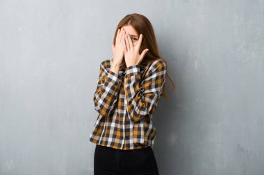 Genç kızıl saçlı kız, grunge duvarın üstünde. Gözleri elleriyle kaplıyor ve parmaklarından bakıyor.