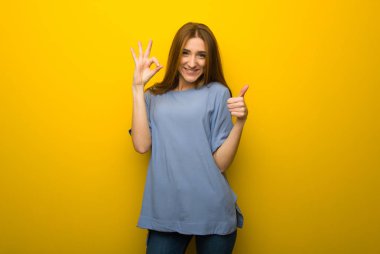 Sarı duvar arka plan gösteren ok işareti ile ve jest bir başparmak veren genç Kızıl saçlı kız