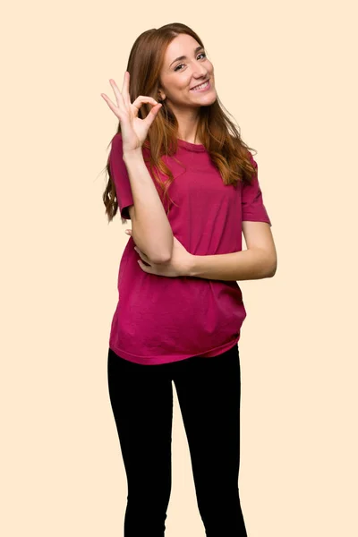 分離された黄色の背景に指で のサインを示す若い赤毛の女の子 — ストック写真