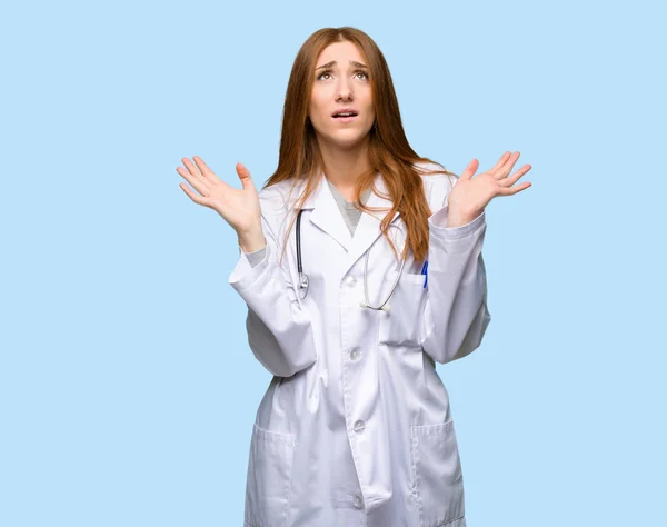 Redhead doctor woman frustrated by a bad situation on isolated blue background