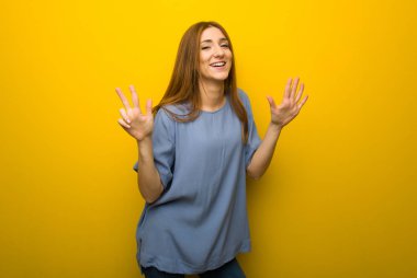 Genç Kızıl saçlı kız sekiz parmak ile sayma sarı duvar arka plan üzerinde