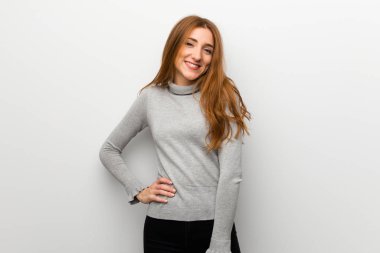 Kızıl saçlı kız kalça, silah ile poz ve gülümseyen beyaz duvar üzerinde