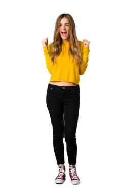 Bir genç kızın sarı kazaklı kazanan pozisyon izole beyaz zemin üzerinde bir zaferini kutluyor tam uzunlukta bir atış