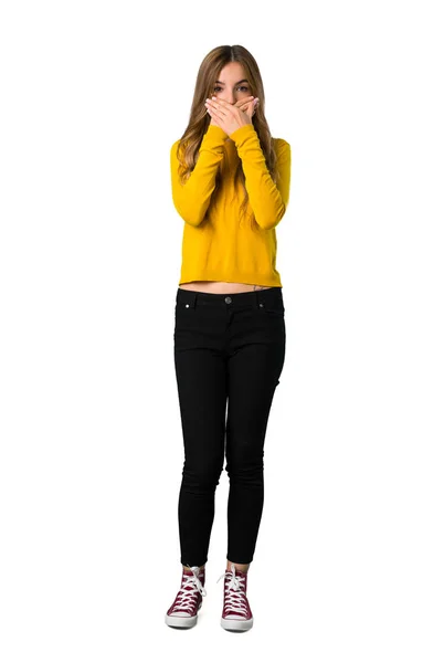 一个年轻女孩的全长照片 照片上的年轻女孩穿着黄色毛衣 双手捂着嘴 因为她在孤立的白色背景上说了一些不恰当的话 — 图库照片