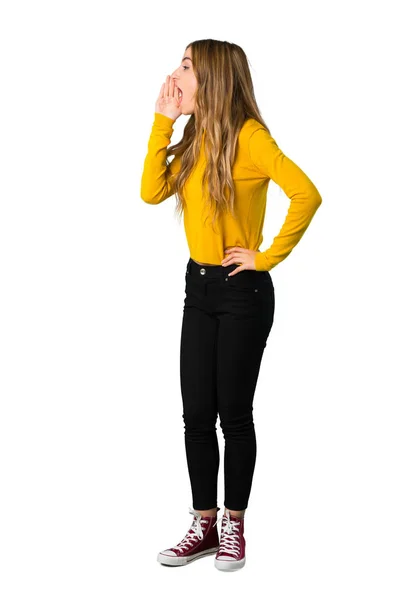 一个穿着黄色毛衣的年轻女孩在孤立的白色背景上张开嘴向侧面喊话的全长照片 — 图库照片