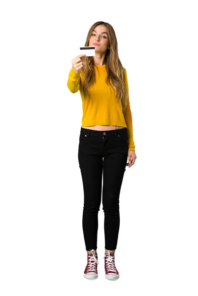 一个穿着黄色毛衣的年轻女孩在孤立的白色背景上拿着信用卡的全长照片 — 图库照片