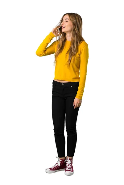 黄色いセーターを着て携帯電話で会話を維持する分離の白い背景の上で若い女の子のフルレングス ショット — ストック写真